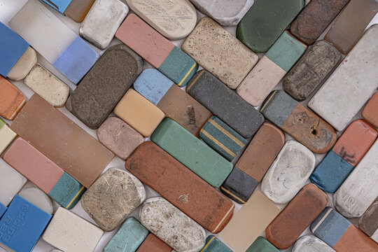 A collection of various used and worn-out erasers, flat lay photograph of a scattered collection of vintage, heavily used, and well-worn rectangular erasers