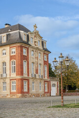 Naklejka premium A large brick building in Munster Germany with a white roof and a red brick facade. The building has a lot of windows and a balcony. The street is empty and the sky is clear.