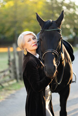 Obraz premium An adult rich woman standing in a park and holding a brown luxury horse