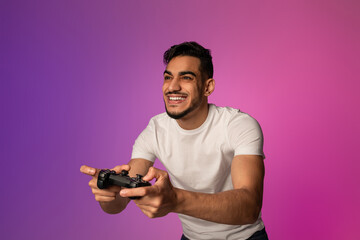 A young Arab man smiles widely while playing video games with a joystick, immersed in a vibrant...