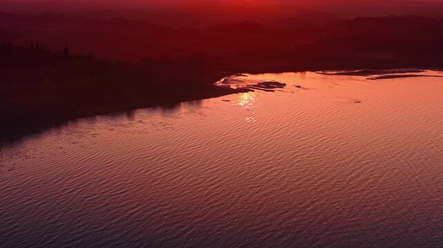 Ridged waterscape colored pink at sunset. Wooded shore is hardly seen in the shade. Aerial view.