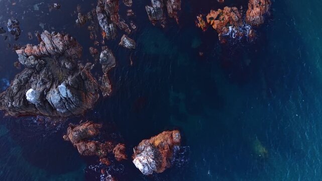 Multiple rocks stick out from dep blue waterscape. Boulders in the sea or ocean water near the coast. Top view.
