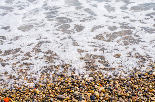 Waves gently washing over a colorful pebble beach on a sunny day - Powered by Adobe