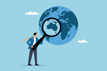 Businessman uses magnifying glass to study globe and discover places