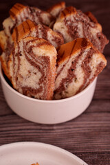 a close-up of a bowl filled with sliced marble cake featuring rich brown and cream swirls. the setting is a rustic wooden surface, creating a warm and inviting atmosphere, decorative, homestyle