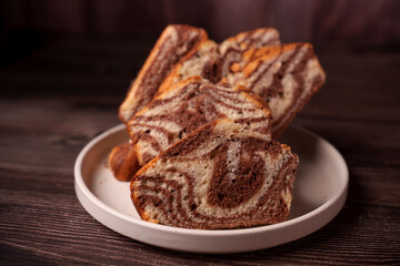 close-up of sliced marble cake on white plate with swirling chocolate and vanilla patterns, set against dark wood background, capturing a cozy and inviting atmosphere, treat, tempting, indulgent