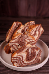 close-up of sliced marble cake on white plate with dark wooden background, highlighting swirled chocolate and vanilla patterns and warm rustic ambiance, platter, earthen, tasty, appeal, visual, art