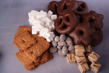 an enticing assortment of holiday cookies and confections, featuring chocolate-covered pretzels, ginger biscuits, marshmallows, sugared almonds, and decorative fudge on a soft, neutral backdrop