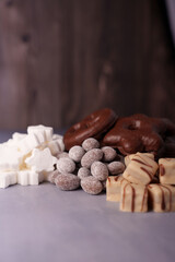 assorted sweets arrangement featuring chocolate-covered pretzels, frosted nuts, fudge pieces, and marshmallow shapes on a textured surface with warm brown backdrop, tasty, crafted, artisan, delicacy