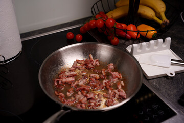 cooking bacon in a stainless steel pan on a modern stovetop with fresh tomatoes and bananas in the background for a cozy, homey kitchen atmosphere, crispy, appetizing, homecooked, warm, delicious