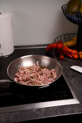 frying bacon strips in a stainless steel pan on a modern stove with fresh vegetables and fruits nearby in a contemporary kitchen setting, spatula, rustic, homestyle, gourmet, textures, metallic