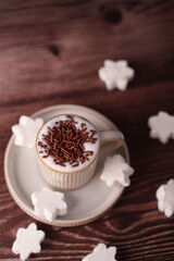 creamy hot beverage in ribbed ceramic cup topped with chocolate sprinkles, surrounded by soft white marshmallows on a warm wooden surface, evoking a cozy, inviting atmosphere, rustic, café, gourmet