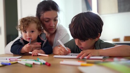 Mother with toddler and older child drawing together at table during calm creative moment as boy concentrates on artwork while baby explores markers in warm-family setting- - Powered by Adobe