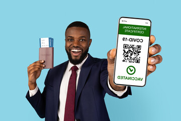 Black Businessman With Passports And Tickets Showing Smartphone With Covid-19 Immune Certificate On Screen, African American Male In Suit Demonstrating QR Code Of Coronavirus Vaccination, Collage