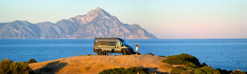 Woman enjoys the Aegean view beside a camper van with Mount Athos in the background. Ideal for:...