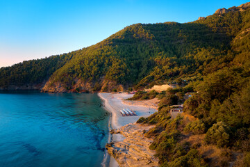 Obraz premium Aerial of Paradise Beach, Thassos Island—turquoise bay, pine hills and white sand at golden hour. Ideal for: Greece travel, beach resorts, summer campaigns.