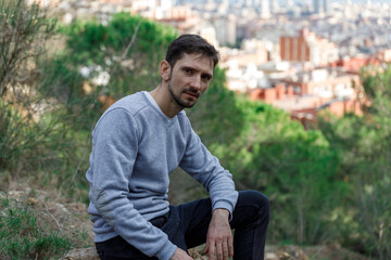 Man is sitting on a hillside, wearing a gray sweater and jeans
