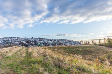 Waste site with workers managing trash during late afternoon in a serene landscape