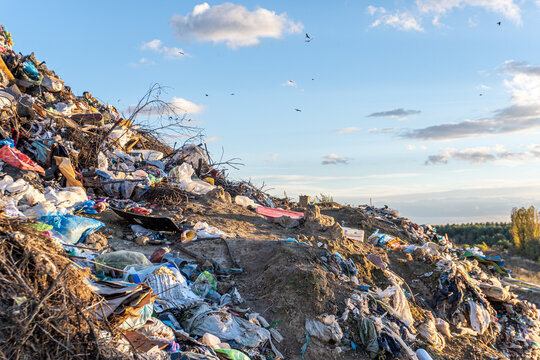 Overgrown landfill at sunset shows neglected waste spilling over the hillside in a rural area