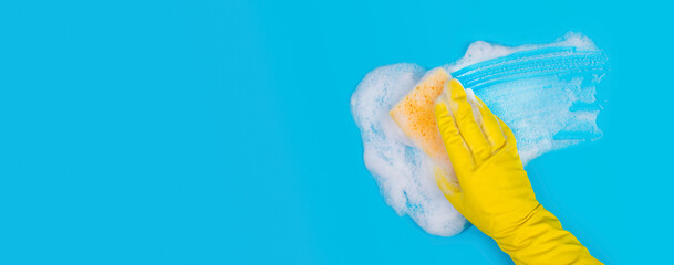 Hand in Yellow Glove Holds Sponge and Wipes Soapy Foam on Blue Background