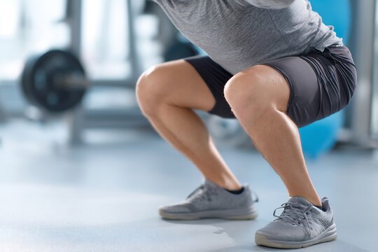 Faceless person performing controlled squat during knee recovery bright gym environment injury rehabilitation concept