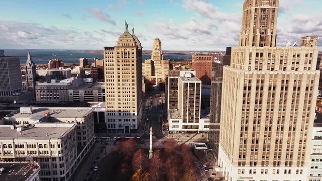 Aerial drone view of downtown Buffalo, New York, featuring a straight-on perspective of a city street lined with tall commercial buildings leading to the iconic Buffalo City Hall. The scene captures u