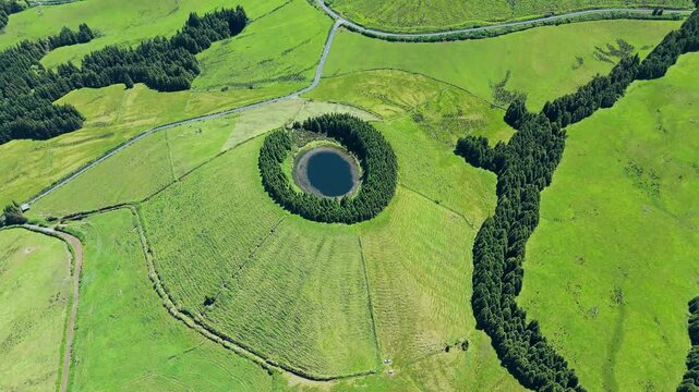 Round Pau Pique volcanic crater lagoon surrounded by lush trees on Sao Miguel. Aerial
