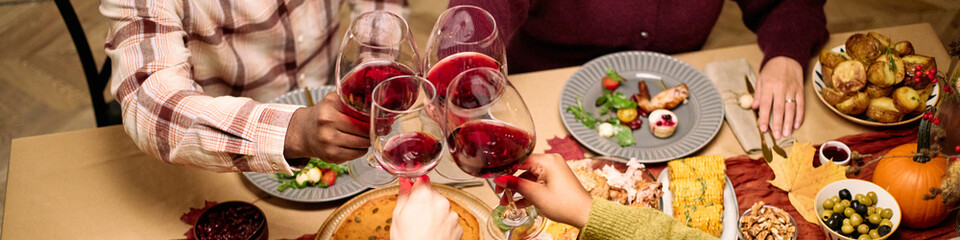 Header of diverse group of young and middle aged friends clinking wine glasses over Thanksgiving...