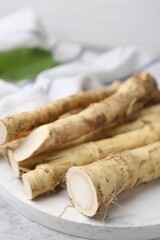 Fresh raw horseradish roots on light grey table, closeup
