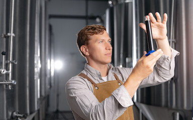 Young caucasian male brewer examining beer sample in modern brewery