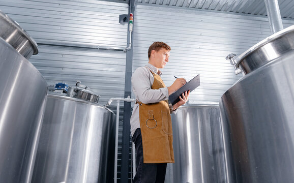 Caucasian male adult brewer inspecting equipment in modern brewery for craft beer. Concept food industry with quality product - Powered by Adobe