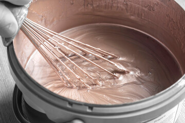 Person stirring mixing gold paint in a plastic paint tub container with a metal whisk. Decorating do it yourself home improvement concept.