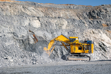 Yellow Excavator Digging in Rocky Quarry Landscape Under Clear Sky