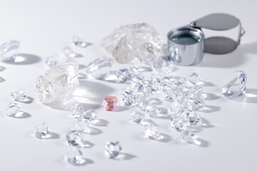 Collection of clear and pink diamonds with jeweler's loupe on white background