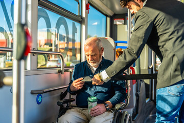 Man helping senior in wheelchair securing safety belt on bus