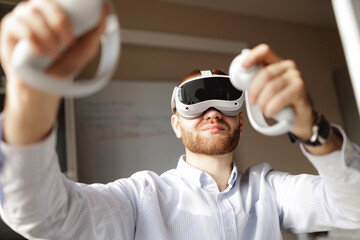 Young caucasian male using virtual reality headset with controllers in office for video presentation of project