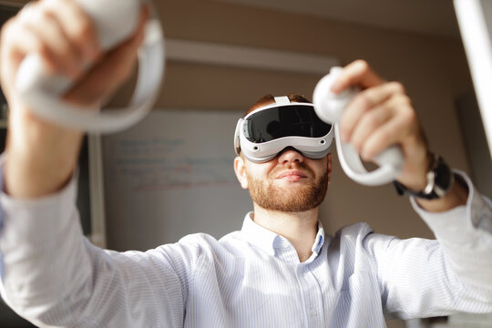 Young caucasian male using virtual reality headset with controllers in office for video presentation of project