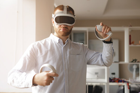 Young caucasian male developer engaging in virtual reality with headset and controllers, sunlight