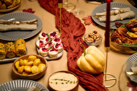 Thanksgiving dinner table featuring roasted turkey, corn on cob, potatoes, pumpkin, assorted desserts, walnuts, hummus, elegant plates and napkins arranged for festive meal among friends - Powered by Adobe