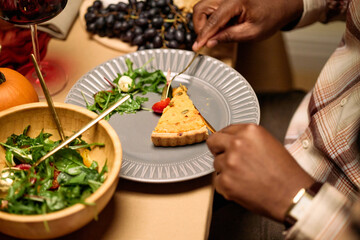 Black man sitting at table eating slice of pie with fork during thanksgiving dinner among friends,...