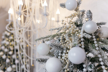 Christmas tree decorated with white and transparent balls made of eco-friendly material in the interior of a residential building against a white wall and fabric.
