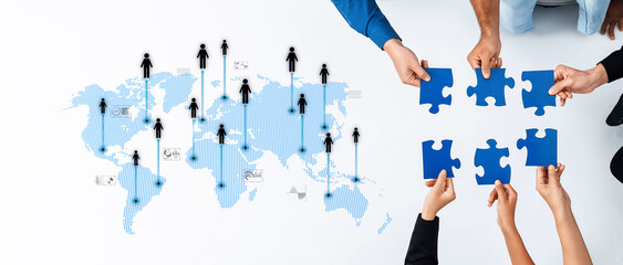 This image showcases hands working together to assemble blue puzzle pieces over a world map, symbolizing collaboration, connection, and strategic teamwork in a globalized environment. Trope