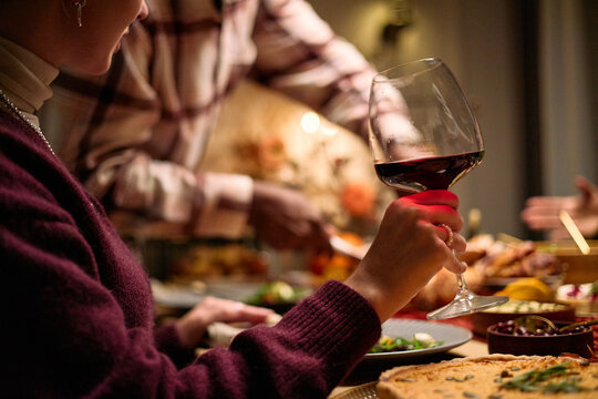 Young adult Caucasian woman holding wine glass while multiethnic young adults serving food at Thanksgiving dinner table, visible hands and partial faces engaging in festive meal sharing - Powered by Adobe