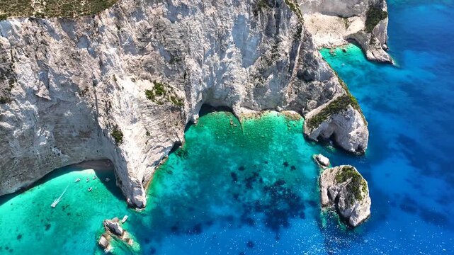 Aerial drone cinematic video of tropical exotic island bay with steep white cliffs and sea caves creating a blue lagoon visited by small tourist boats