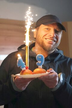 Smiling man celebrating 49th birthday with cake, candles, and a sparkling sparkler