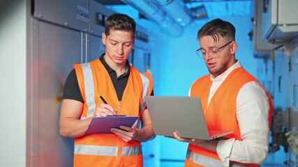Two engineers collaborate in server room. Professionals discuss data on laptop, taking notes. Demonstrates teamwork, focus, diligence. - Powered by Adobe