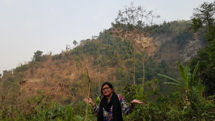 Joyful woman posing with a radiant smile amidst a dry, rugged hilly landscape under a bright, clear sky