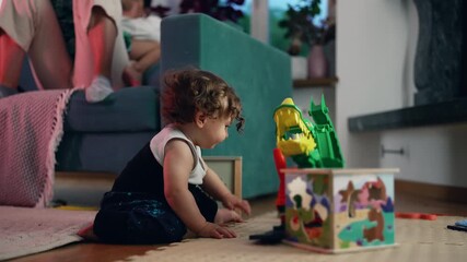 Toddler stretches toward playful alligator toy on activity box during energetic moment of discovery showing curiosity determination and joyful engagement in bright indoor family environment