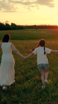 Parent mommy child together in nature. Joyful family strolls through sunlit meadow. Mother child daughter frolic on verdant grass. Mom little daughter are out in nature. Family outing. Day of freedom