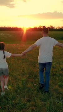 Joyful family strolls through a sunlit meadow. Father child daughter frolic on verdant grass. Dad little daughter are out in nature. Family outing. Day of freedom. Parent dad child together in nature